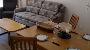 Uma sala de estar com sofá, mesa de jantar com cadeiras, luminária e um quadro na parede.