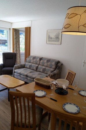 Ein Wohnzimmer mit einer Couch, einem Esstisch mit Stühlen, einer Lampe und einem gerahmten Bild an der Wand.
