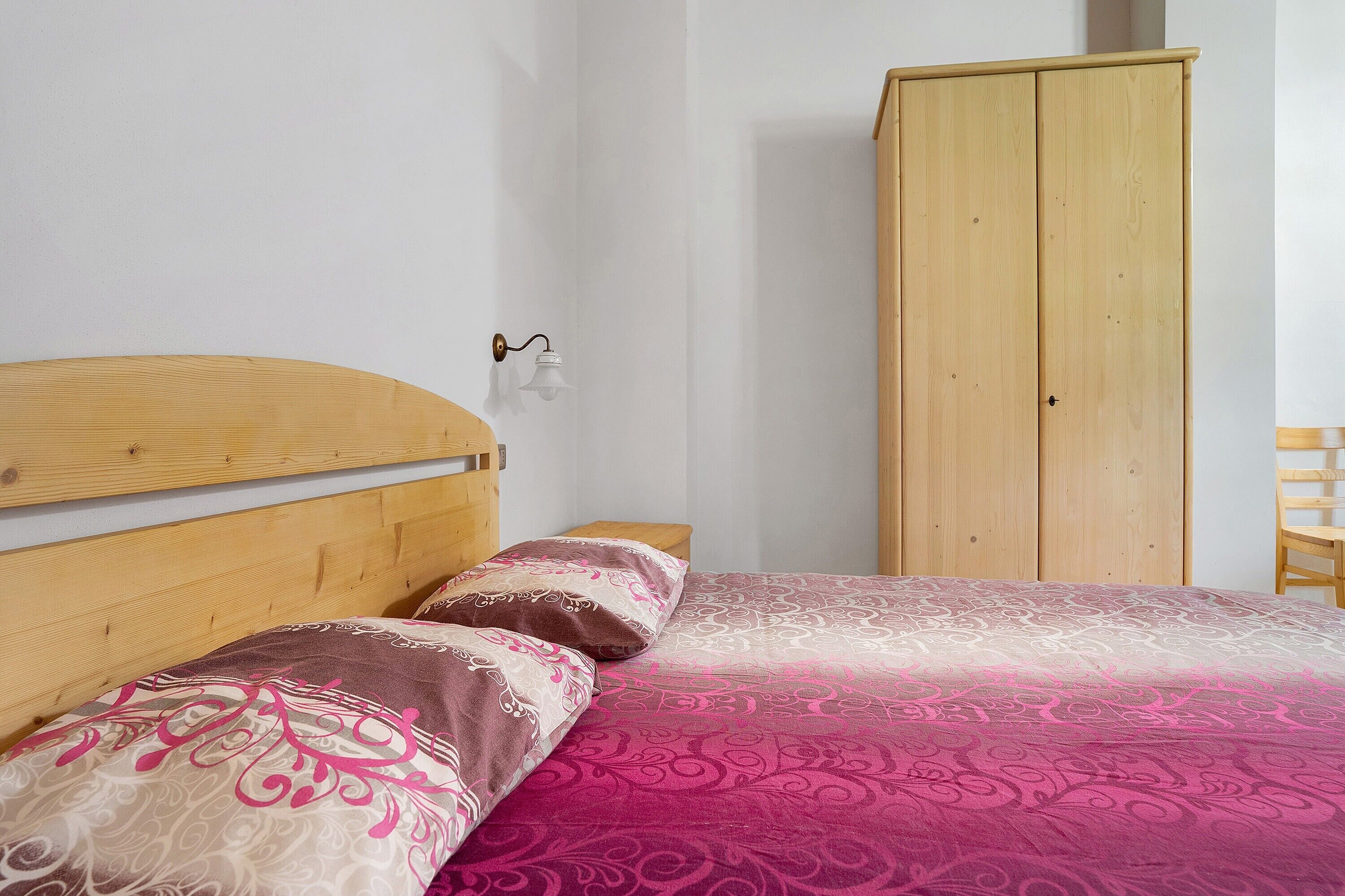 Un dormitorio con cabecera de madera, cama con ropa de cama estampada, mesita de noche y armario de madera.