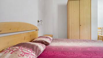 Un dormitorio con cabecera de madera, cama con ropa de cama estampada, mesita de noche y armario de madera.