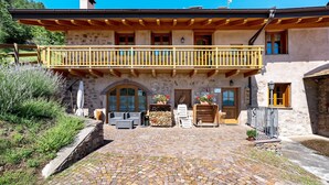 A stone building with a wooden balcony, outdoor seating, and a stone wall.