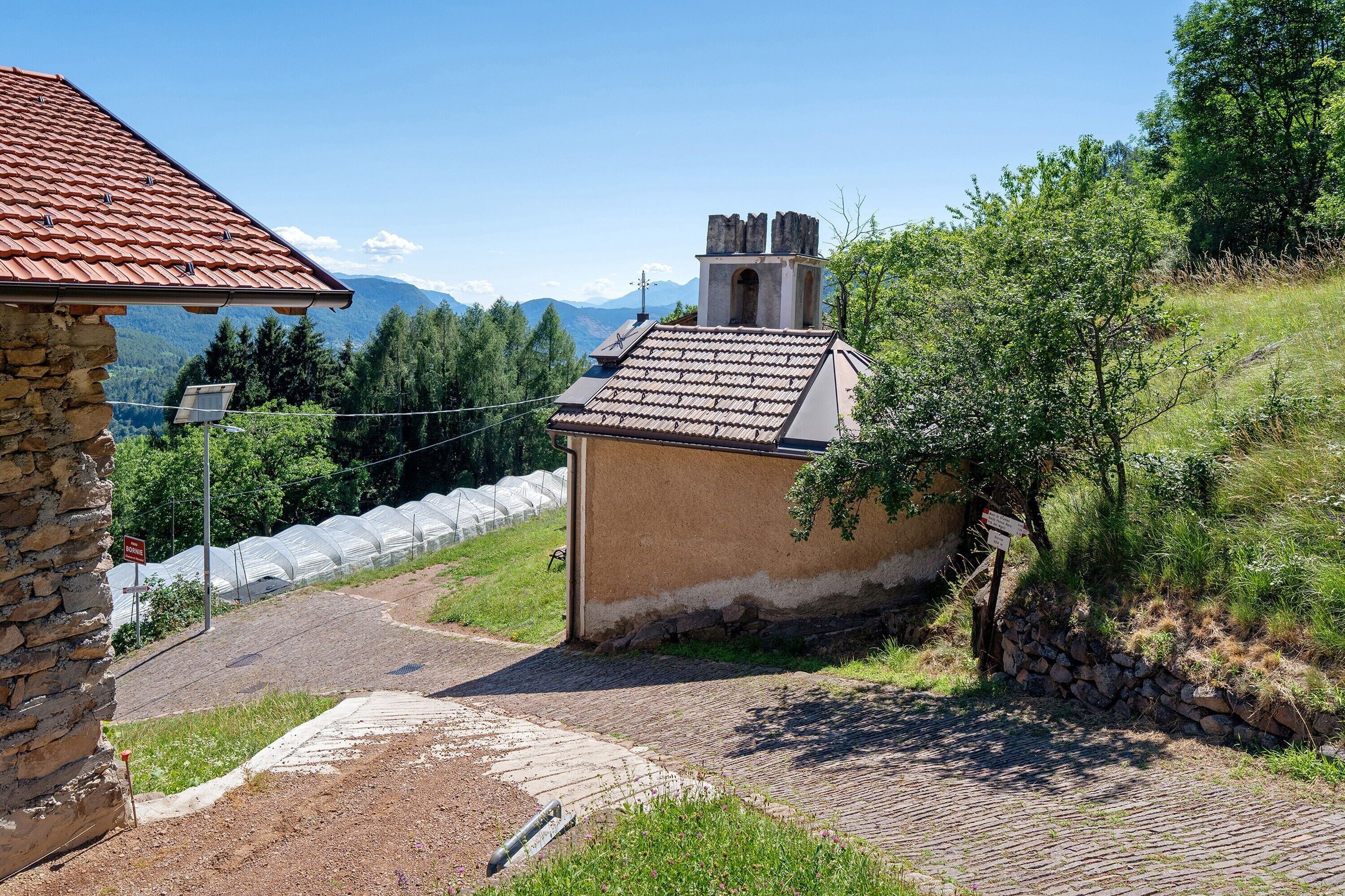 Un edificio de piedra con tejado de baldosas, una pared de piedra y un camino empedrado que conduce a una zona verde con árboles.