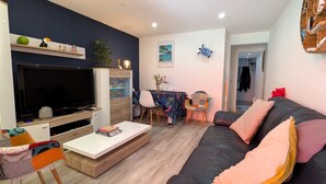 Een woonkamer met een flatscreen televisie, een bank, een salontafel en een eethoek met stoelen.
