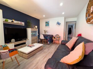 Ein Wohnzimmer mit Flachbildfernseher, einer Couch, einem Couchtisch und einem Essbereich mit Stühlen.