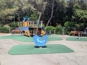 Ein Spielplatz mit Klettergerüsten, einer Bank und grünem Kunstrasen.