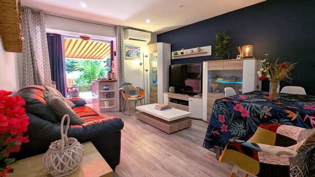 Een moderne woonkamer met een bank, salontafel, televisie en een eethoek met een tafel en stoelen.
