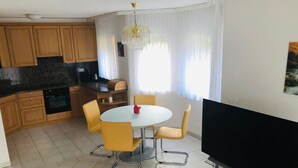 Une cuisine moderne avec des meubles en bois, une table à manger avec des chaises jaunes, un téléviseur à écran plat et un lustre.