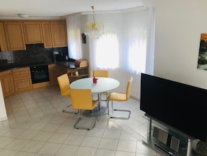 A modern kitchen with wooden cabinets, a dining table with yellow chairs, a flat-screen TV, and a chandelier. - Edelweiss B 23 # 4-bed apartment, Dusche, WC 4-bed apartment, Dusche, WC by Interhome (Leukerbad)