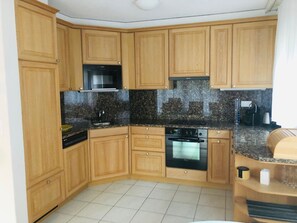 A compact kitchen with wooden cabinets, a built-in oven, and a granite countertop. - Edelweiss B 23 # 4-bed apartment, Dusche, WC 4-bed apartment, Dusche, WC by Interhome (Leukerbad)