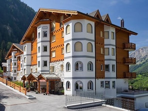 A multi-story hotel with a reception area, balconies, and a mountainous backdrop. - Edelweiss B 23 # 4-bed apartment, Dusche, WC 4-bed apartment, Dusche, WC by Interhome (Leukerbad)