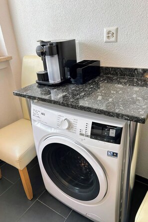 A front-loading washing machine with a coffee maker on top, a chair, and a power outlet on the wall. - Salve 3 # 4-bed apartment, Dusche, WC 4-Bettwohnung, Dusche, WC by Interhome (Leukerbad)