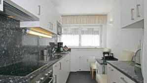 A modern kitchen with a black granite countertop, stainless steel appliances, and a window with sheer curtains. - Salve 3 # 4-bed apartment, Dusche, WC 4-Bettwohnung, Dusche, WC by Interhome (Leukerbad)