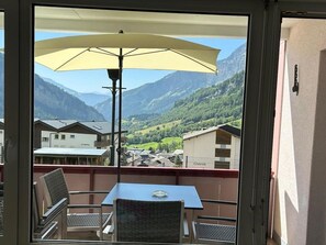 A balcony with a table and chairs, a yellow umbrella, and a view of a mountain village. - Salve 3 # 4-bed apartment, Dusche, WC 4-Bettwohnung, Dusche, WC by Interhome (Leukerbad)