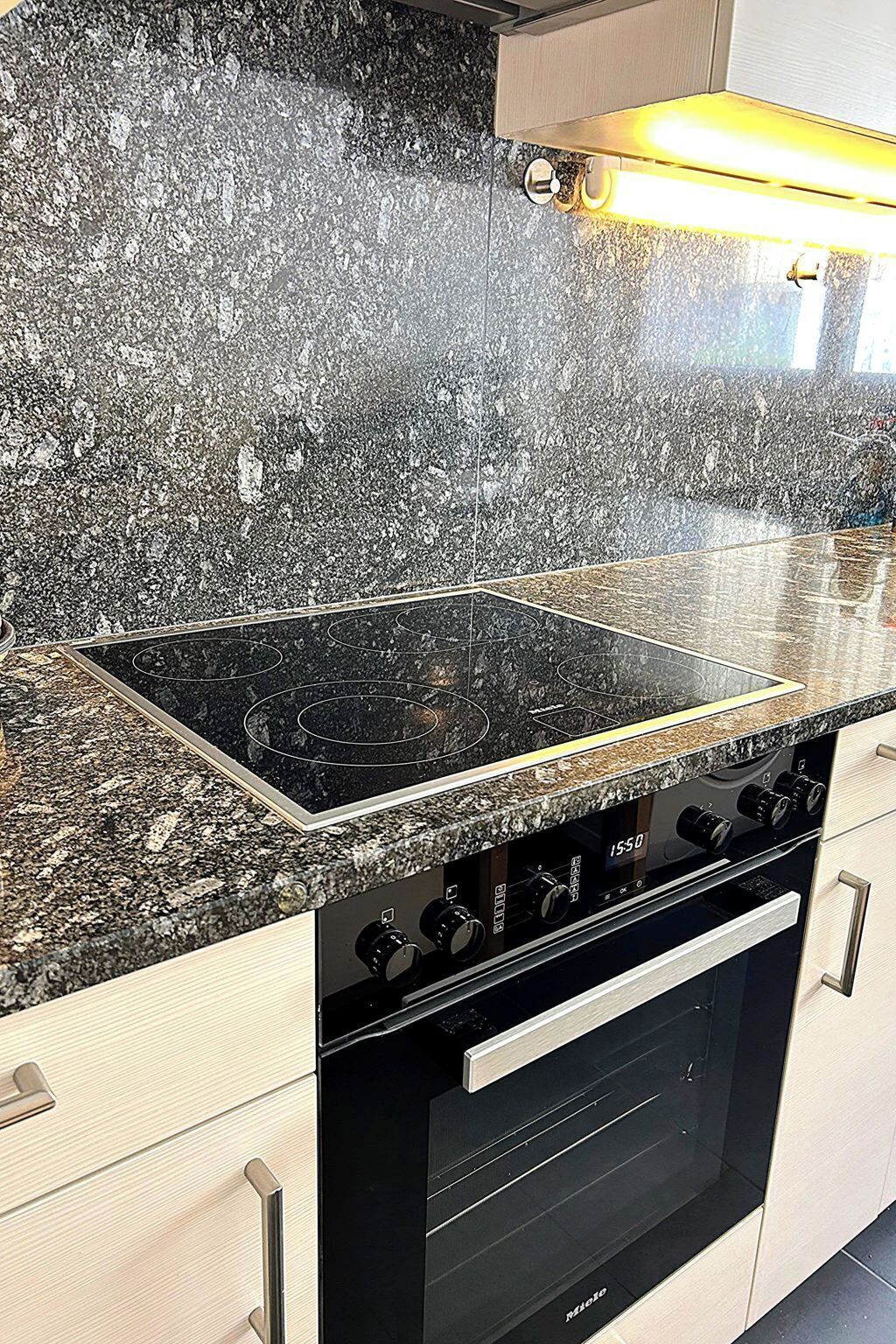 Una cocina con encimera de granito, estufa negra y horno empotrado.