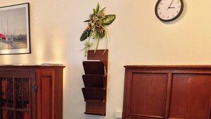 A dining area with a table covered in a floral tablecloth, a bottle of liquor, a clock on the wall, and a wooden cabinet. - Salve 3 # 4-bed apartment, Dusche, WC 4-Bettwohnung, Dusche, WC by Interhome (Leukerbad)