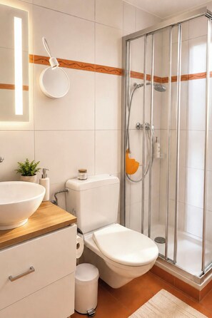 Et moderne badeværelse med et glas brusekabine, et hvidt toilet, et træbord med en stor vask og en lille potteplante.