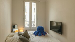 A bedroom with a bed, pillows, a blue octopus plush toy, a TV on the wall, and a window with a balcony. - Spacious apartment right by Clichy Park (Paris)