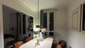 A dining area with a round table, chairs, a candle, a vase with flowers, and a lamp. - Spacious apartment right by Clichy Park (Paris)