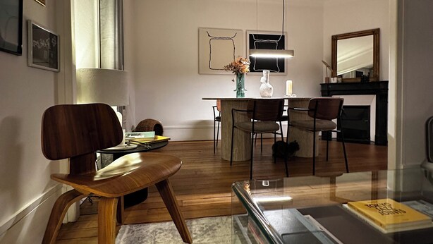 A modern living room with a wooden chair, a glass coffee table, and a dining area with a table and chairs. - Spacious apartment right by Clichy Park (Paris)