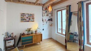 A room with exposed wooden beams, a sofa, a table, a bookshelf, and a window with curtains. - Nice Apartment Near Buttes Chaumont (Paris)