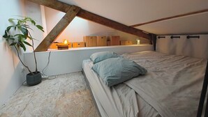 A bedroom with a sloped ceiling, a bed with pillows, a bedside table with a lamp, and a potted plant. - Nice Apartment Near Buttes Chaumont (Paris)