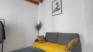 A room with a grey sofa, a black table, wooden beams on the ceiling, and a framed picture on the wall. - Nice Apartment Near Buttes Chaumont (Paris)