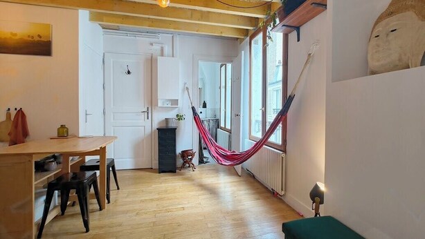 A room with a wooden floor, a hammock, a green sofa, and a white door. - Nice Apartment Near Buttes Chaumont (Paris)