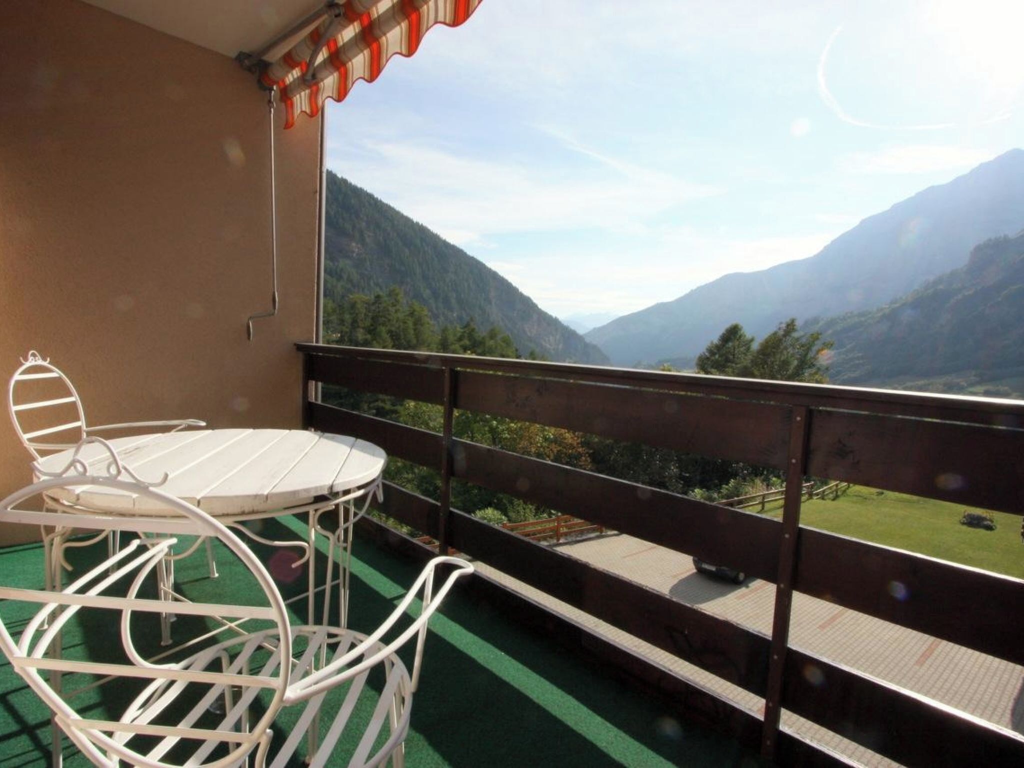 A balcony with a table and chairs, overlooking a mountainous landscape.