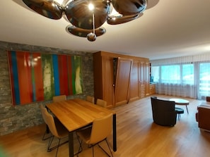 Eine moderne Küche mit Holztisch und -stühlen, einem farbenfrohen abstrakten Gemälde an der Wand und einem großen Fenster mit Vorhängen.