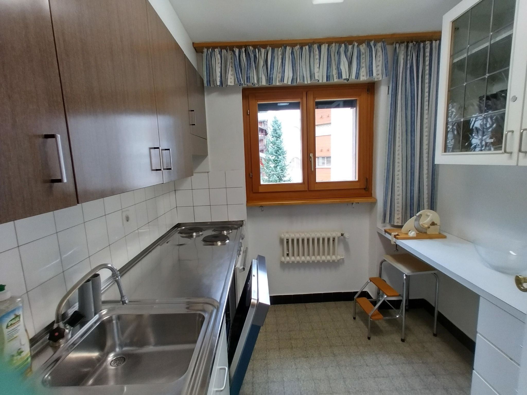 A kitchen with a stove, sink, and window with curtains.