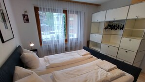 Ett sovrum med två sängar, en garderob och ett fönster med tunna, genomskinliga gardiner.