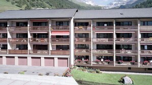 Ett hotell med flera våningar, balkonger, en parkeringsplats och en bergig bakgrund.