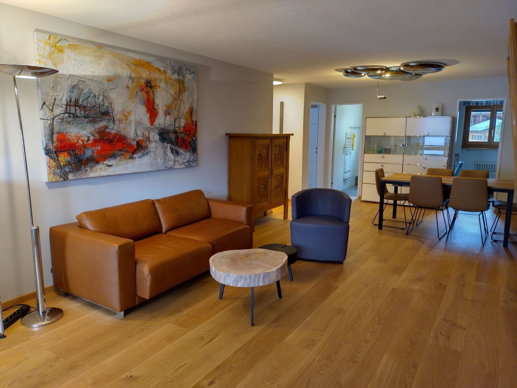 Ein Wohnzimmer mit einer Couch, einem runden Couchtisch, einem blauen Sessel und einem Essbereich mit Stühlen und Tisch.