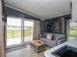 Uma sala de estar moderna com um sofá cinza, uma mesa de centro de madeira e um grande painel de vidro deslizante que dá para um deck externo.
