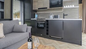 Una cocina moderna con horno empotrado, microondas y hervidor, un sofá gris y una botella de vino sobre una mesa de madera.