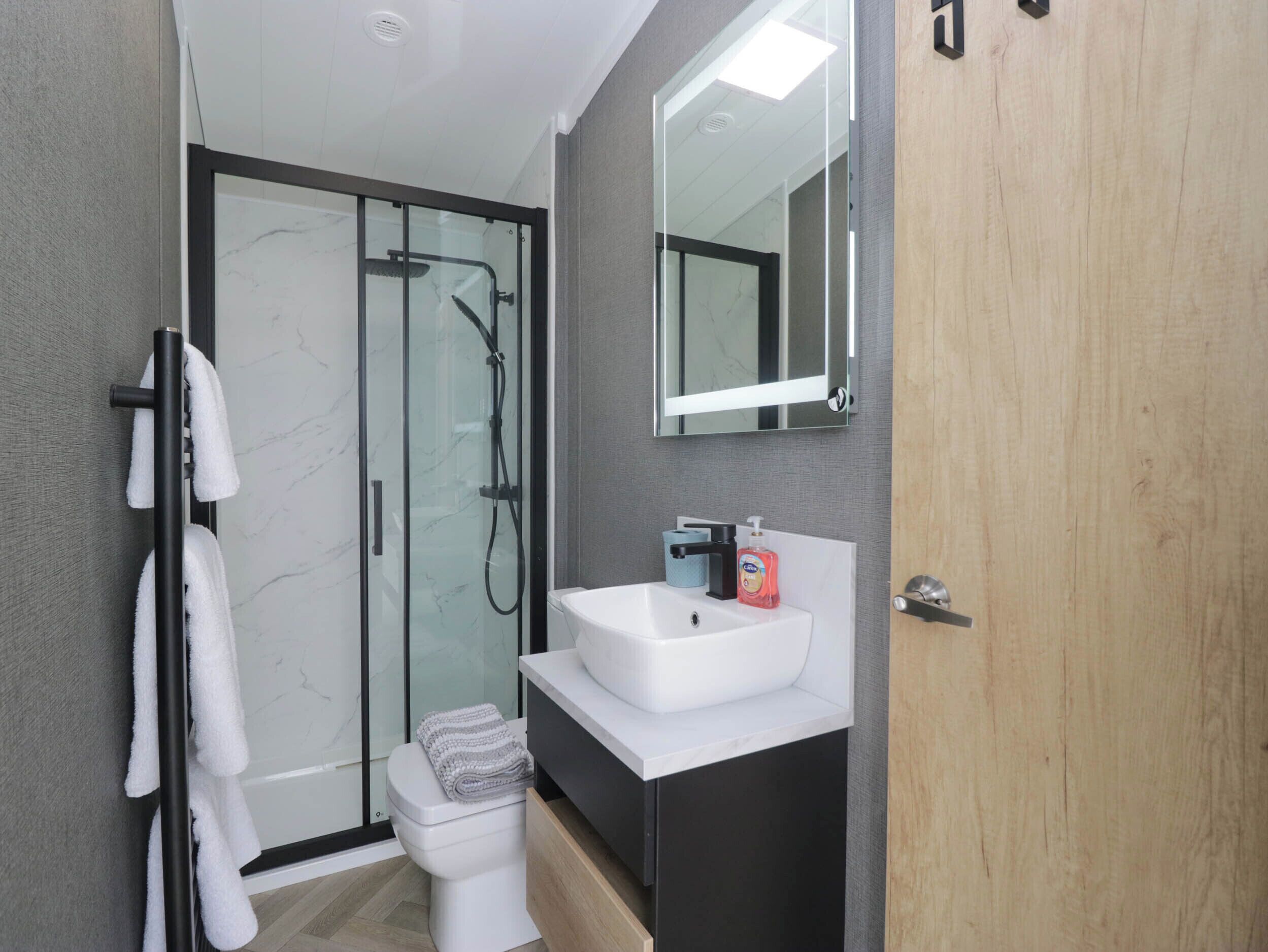 Un baño moderno con ducha envuelta en cristal, un lavabo blanco y una puerta de madera.