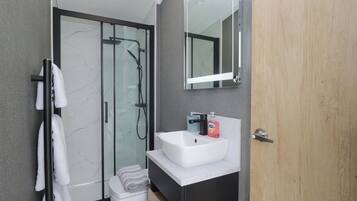 Un baño moderno con ducha envuelta en cristal, un lavabo blanco y una puerta de madera.