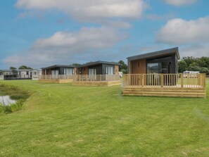 A row of modern mobile homes with wooden decks and large windows, set in a grassy area with a clear sky.