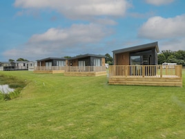 A row of modern mobile homes with wooden decks and large windows, set in a grassy area with a clear sky.