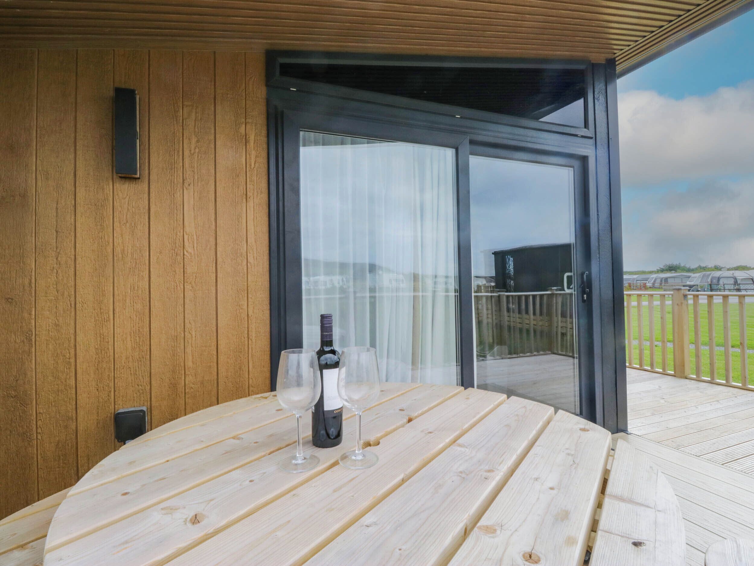 Una terraza de madera con una mesa, una botella de vino y dos copas.