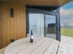 A wooden deck with a table, a bottle of wine, and two glasses. - Heron (Millom)