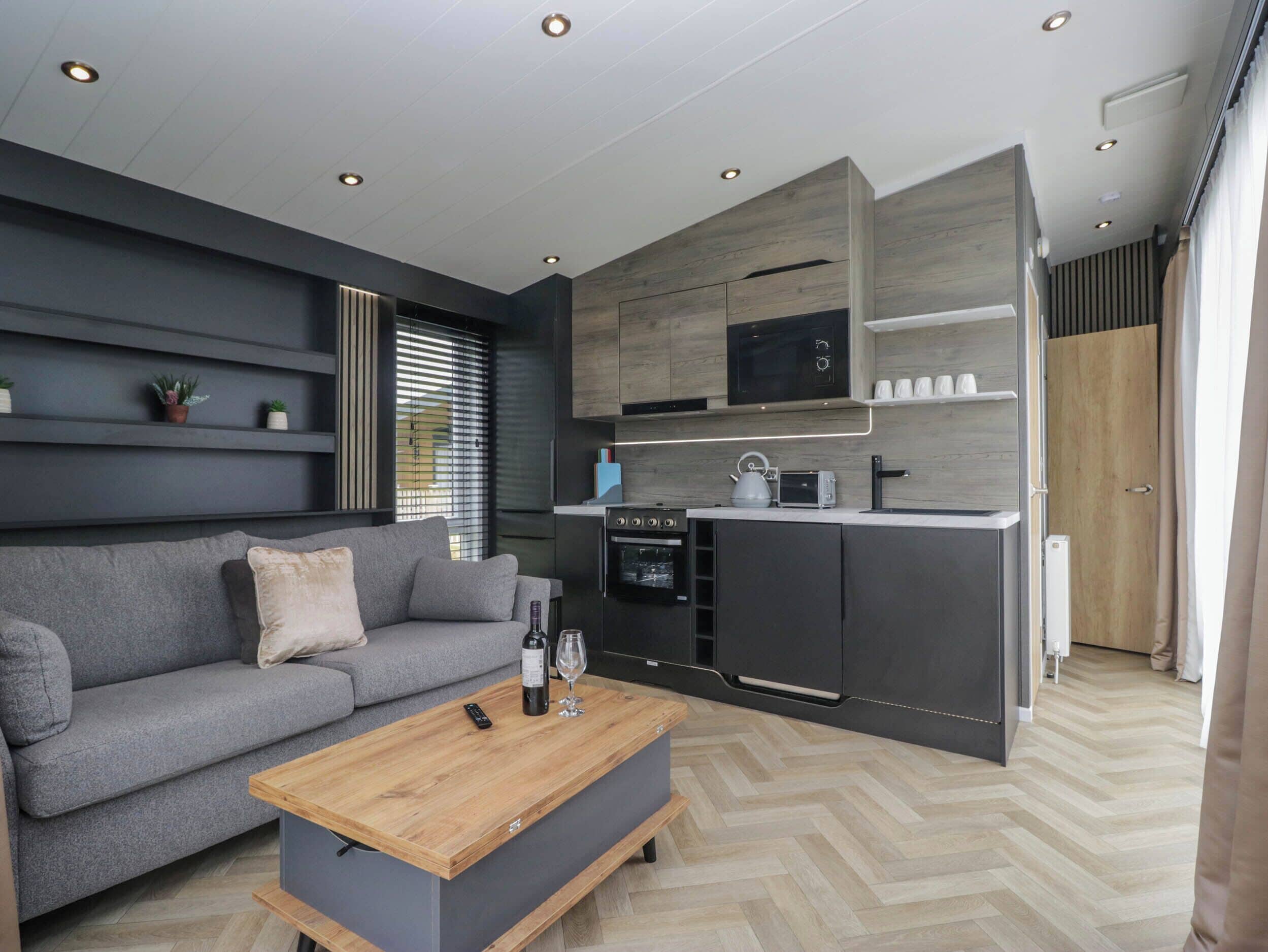 A modern kitchen with built-in appliances, a grey sofa, and a wooden coffee table.