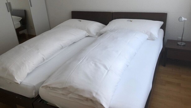 Ein Doppelbett mit weißer Bettwäsche in einem Hotelzimmer.