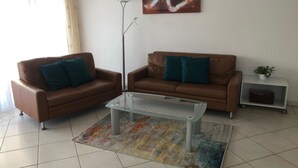 Ein Wohnzimmer mit zwei braunen Ledersofas, einem Glastisch und einem farbenfrohen Teppich.