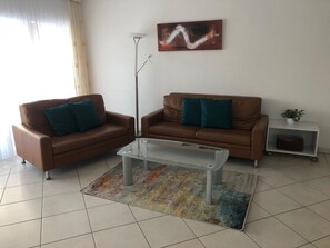 Ein Wohnzimmer mit zwei braunen Ledersofas, einem Glastisch und einem farbenfrohen Teppich.