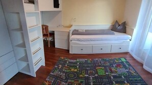 Een slaapkamer met een bed, een bureau, een stoel, een kledingkast en een kleurrijk vloerkleed.