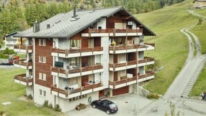 Een meerlaags chalet met balkons, gelegen in een bergachtig gebied met een weg in de buurt.