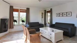 A living room with a sofa, a coffee table, a wicker chair, and a fireplace. - Romantic Villa for 2-guests With Sauna, Makkum (Makkum)