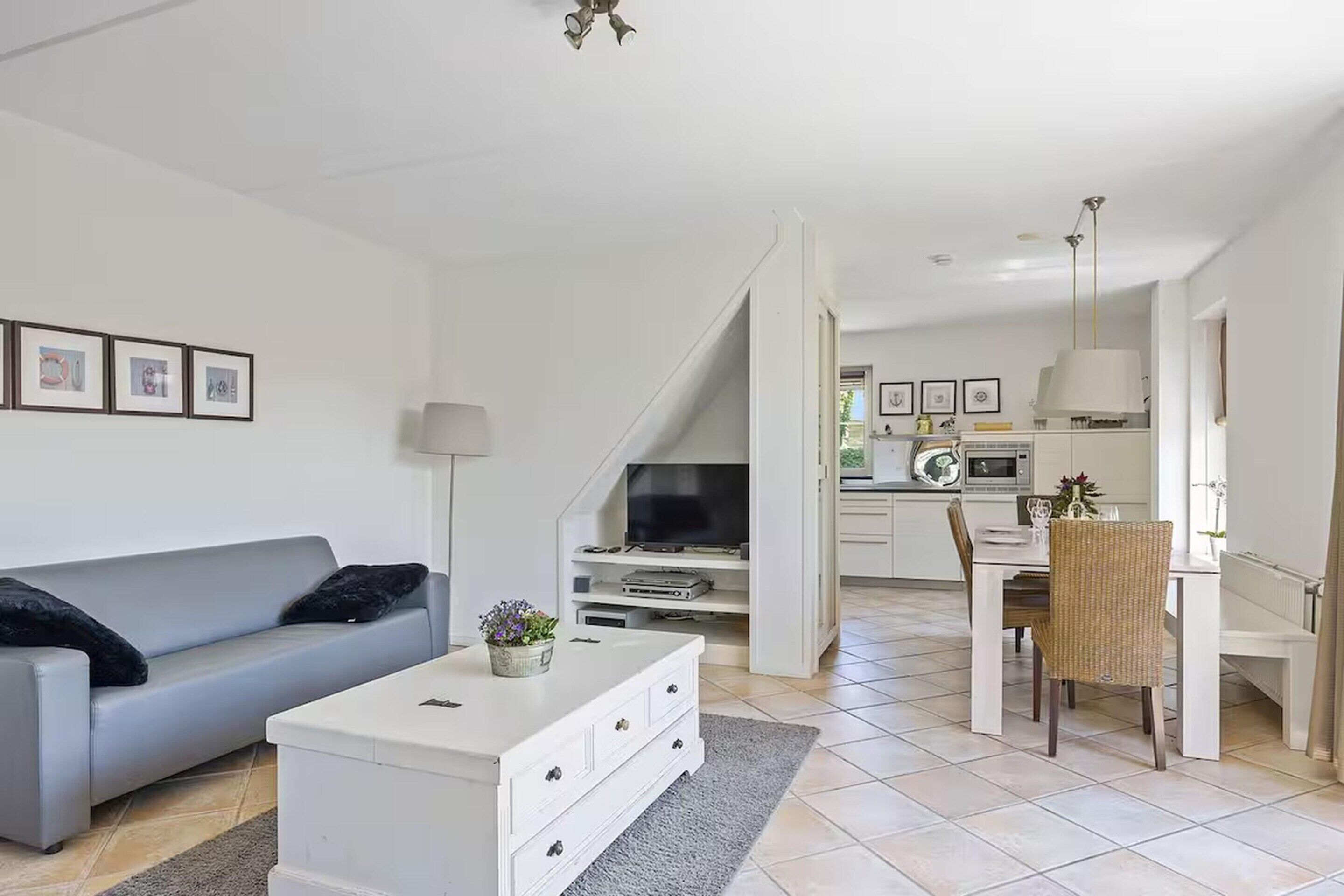Una sala de estar moderna con un sofá gris, una mesa de centro blanca y una zona de comedor con mesa y sillas.