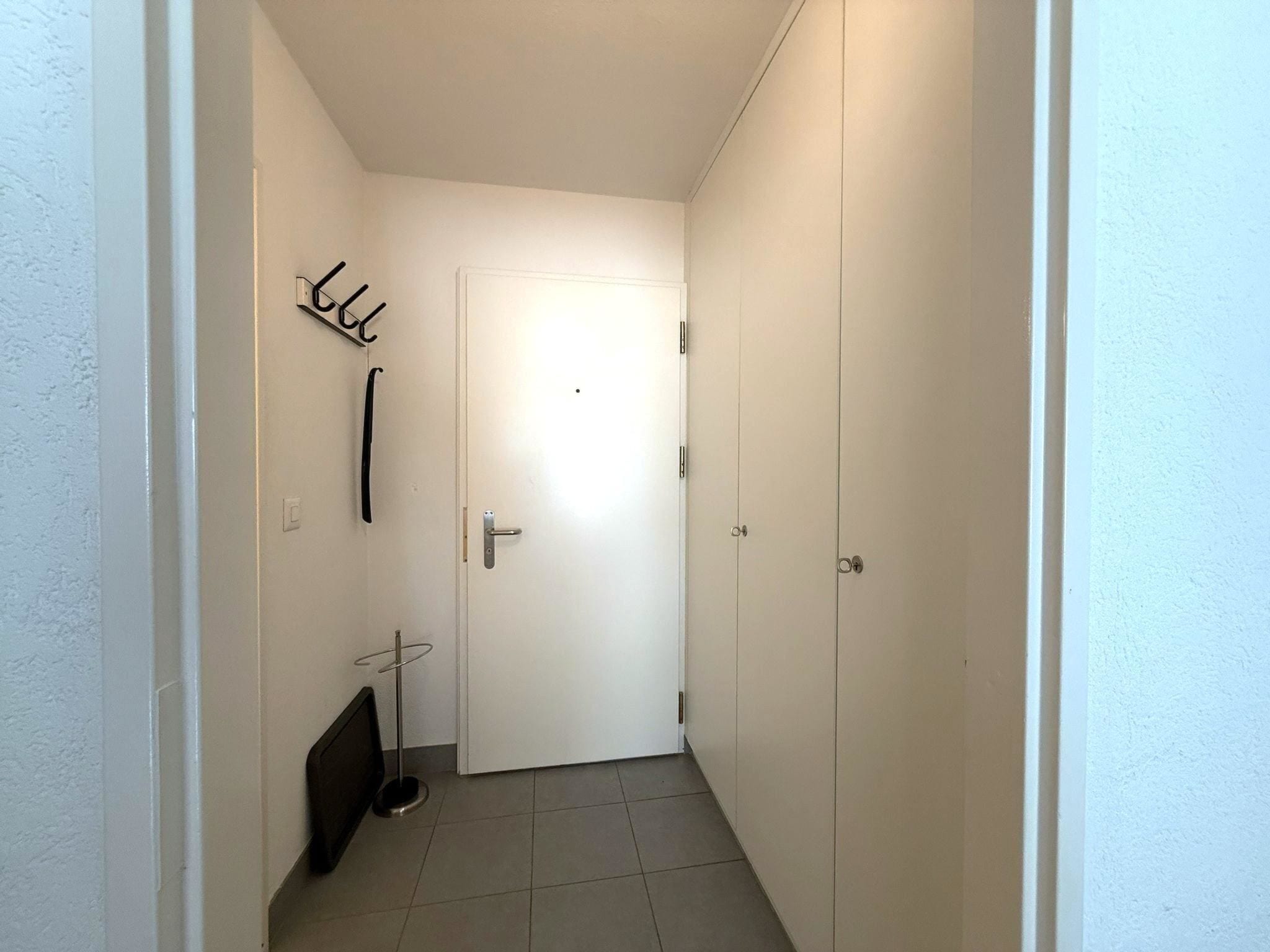 A narrow hallway with a white door, a coat rack, and a radiator.